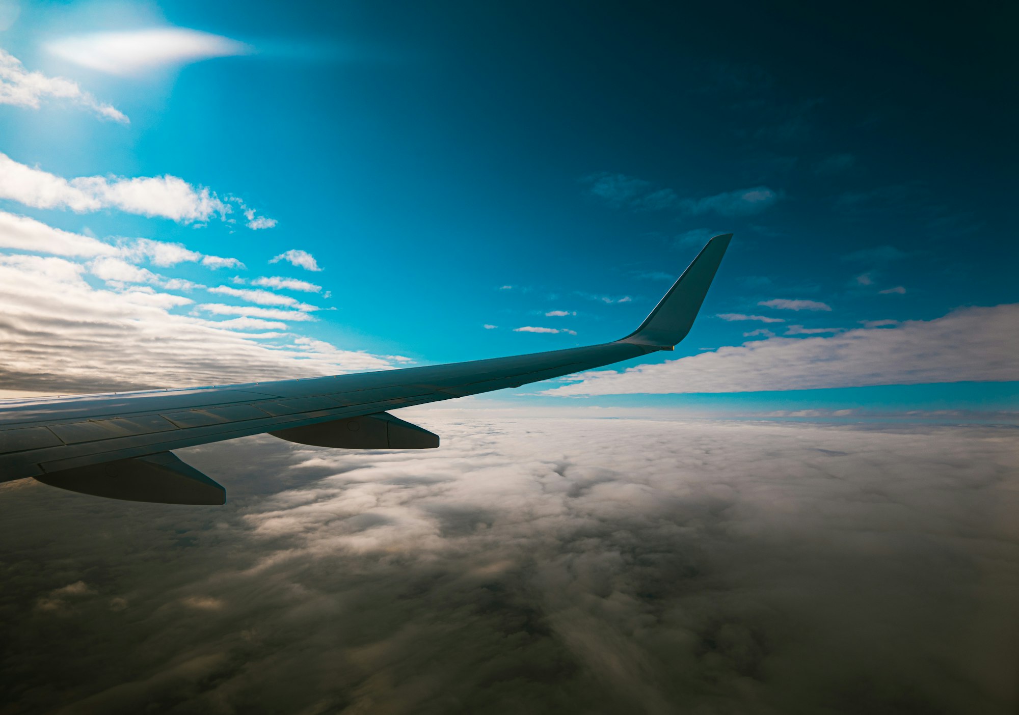 機艙窗外望向客機機翼,機翼下方是大片雲海,上方是無雲的深藍天空