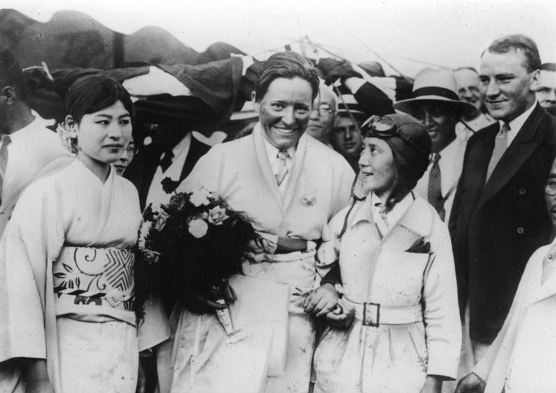 1931 年東京，Marga von Etzdorf 穿著和服式的外袍、捧著一束花，站在人群中間笑著，左邊是穿和服的女性，右邊是一位戴飛行帽的女性