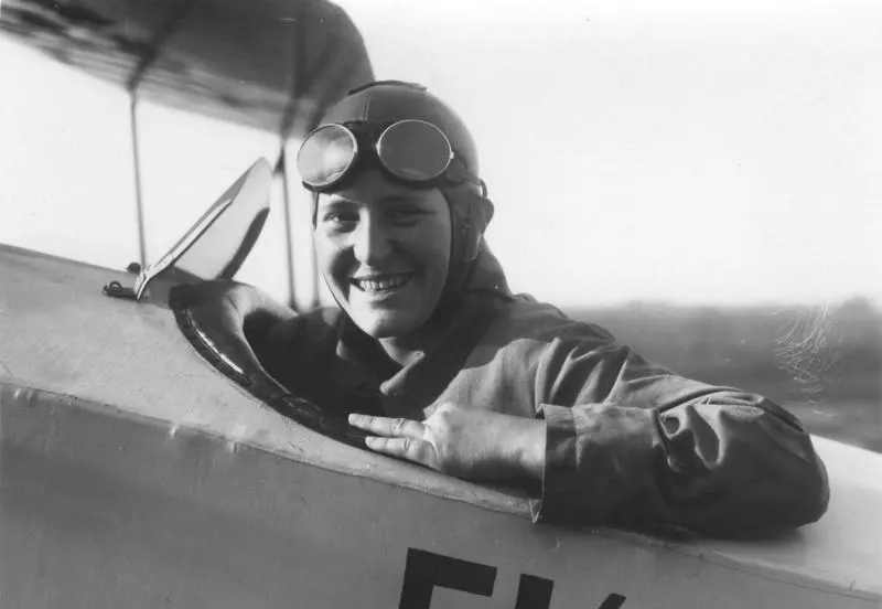 1930 年的黑白照片，Marga von Etzdorf 坐在一架雙翼機的開放式座艙裡，戴著皮製飛行帽，護目鏡推到額頭上，穿著飛行夾克，手搭在座艙邊緣笑著