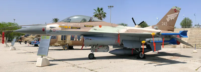 戶外展場上一架沙漠迷彩塗裝的以色列空軍 F-16A，尾翼與機腹油箱漆著編號 243，座艙下方漆著一個圓形徽記與一個三角形標記