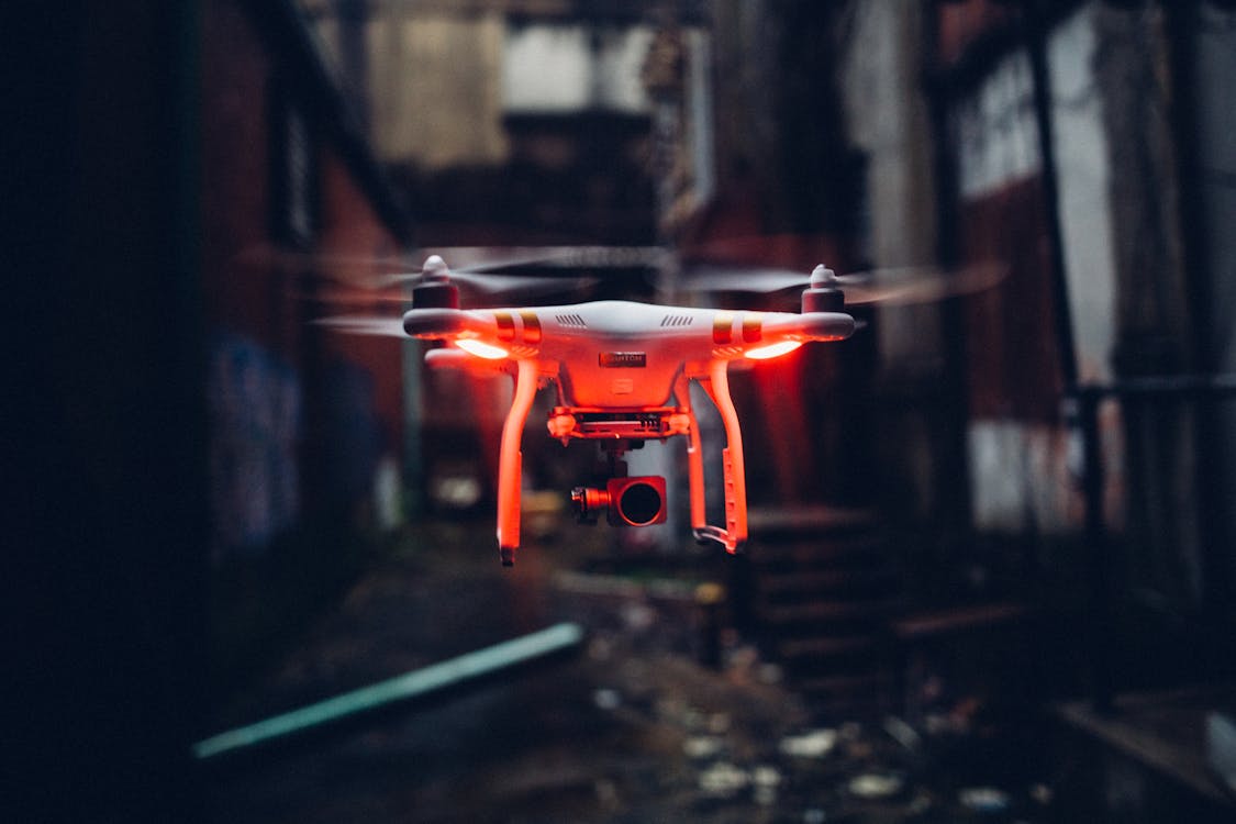 一架帶有紅色燈光的無人機在幽暗的工業街道中低空飛行