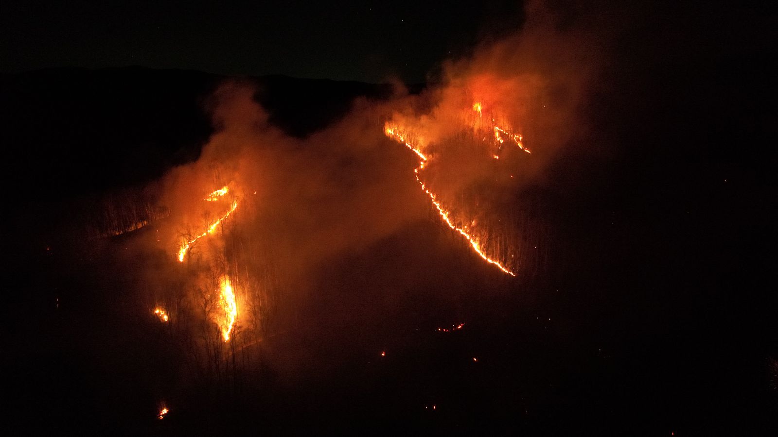 夜間空拍的野火，火線沿著山坡分裂成數道細長火舌